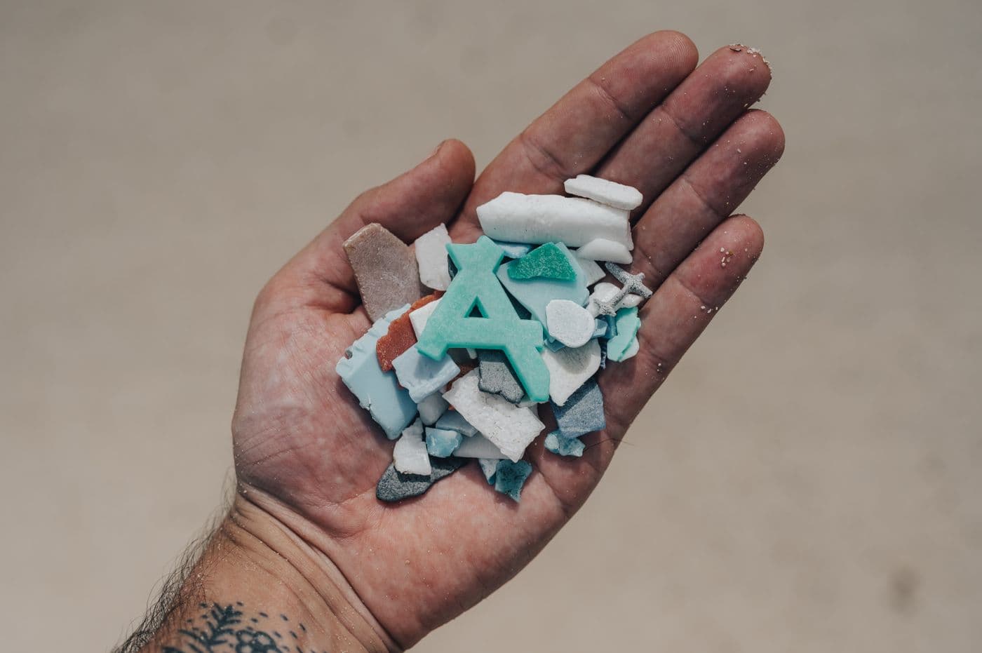 Mano con guante azul sosteniendo fragmentos de microplásticos de colores